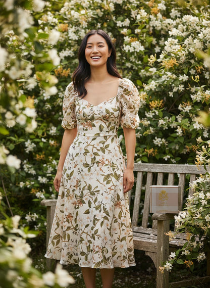 Paradime Enterprise LLC Abbey perfume bottle on a wooden bench next to a woman in a floral dress in a garden