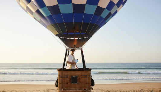 Paradime Enterprise LLC Kanon Elements Air fragrance held by a man in a hot air balloon basket on a sandy beach.